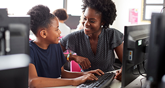 adult helping elementary student in computer lab